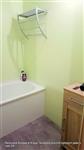 Pohled na koupelnu po renovaco v pastelově zelené barvě s bílou vanou nad ní chromovaná polička a vedle vany světle hnědá komoda z KIKA za 1500Kčs vanou a komodou