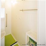 Renovace jádra Koubek - Moderně zrenovovaná umakartová koupelna, bytového panelákového jádra v barvě bílé, zelené lino a kovové doplňky s bílým plastovým regálem na odkládání pracích a čistících prostředků